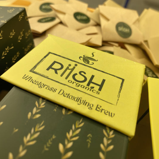 Yellow package of Riish Organics Wheatgrass Detoxifying Brew with green tea bags in the background.